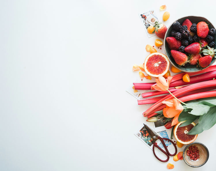 Assorted fruits and vegetables including berries, rhubarb, and oranges on a white background